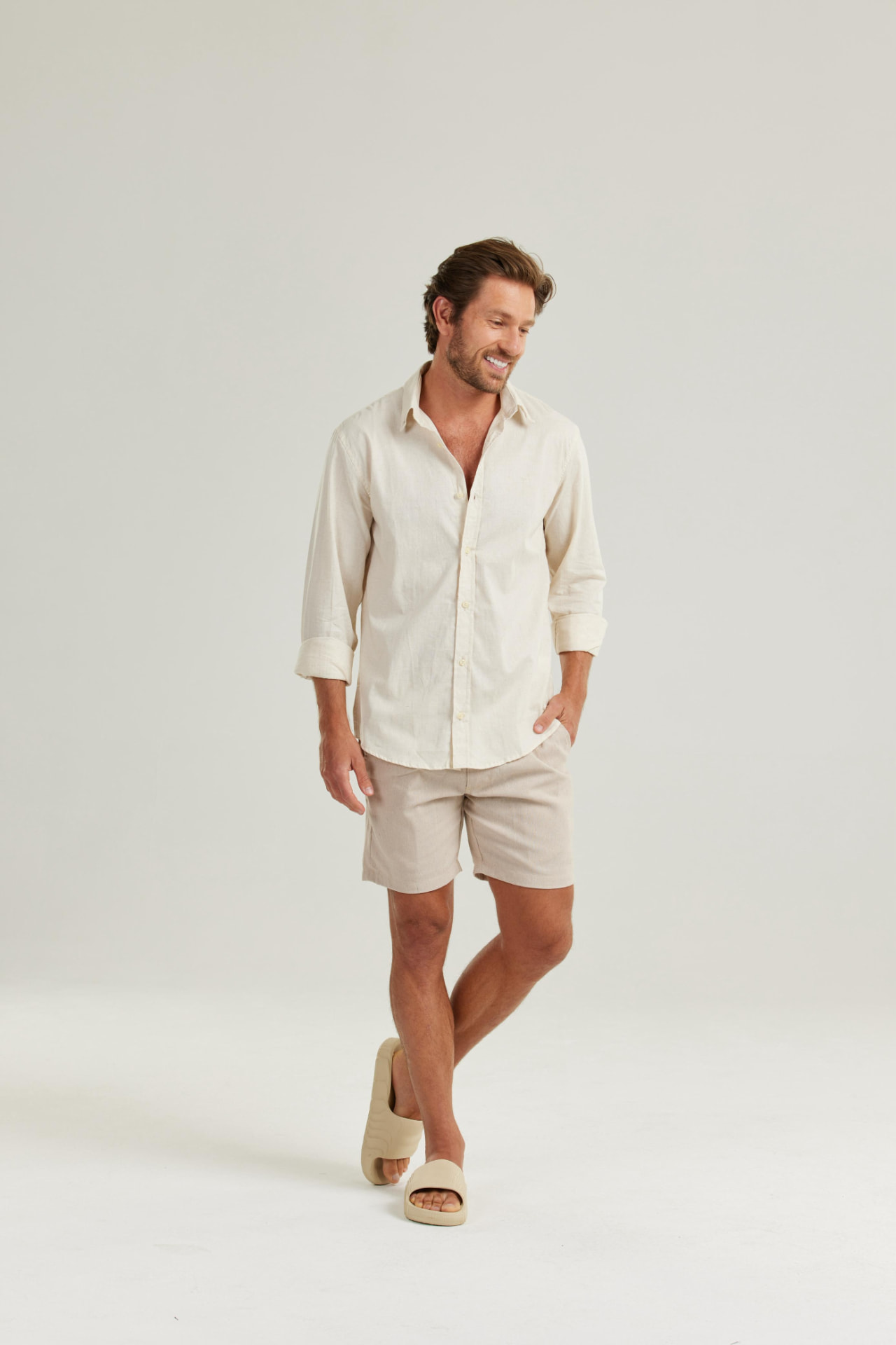 Modelo masculino com camisa e bermuda claras em fundo neutro