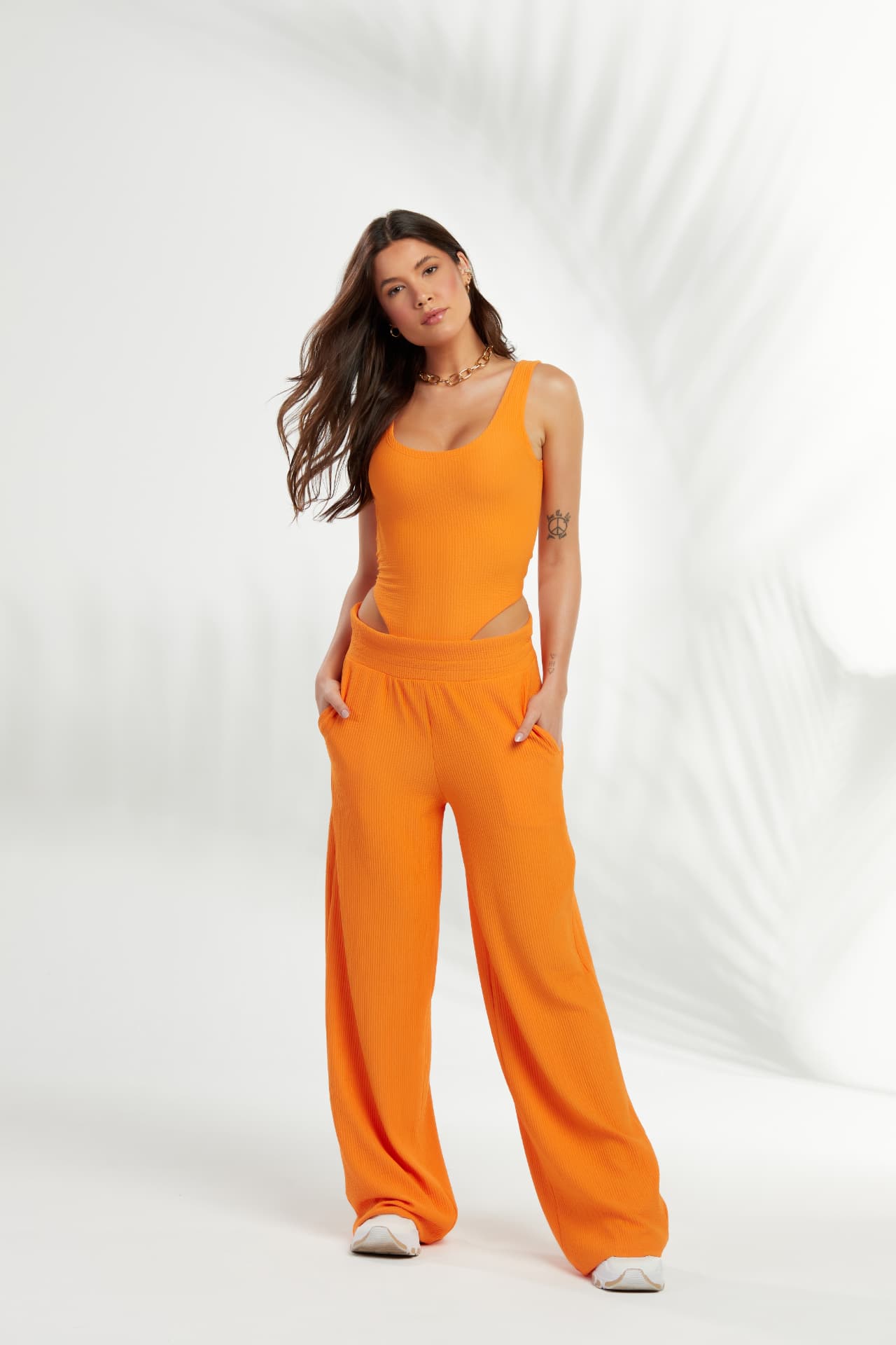 Modelo com body e calça pantalona laranja em fundo branco