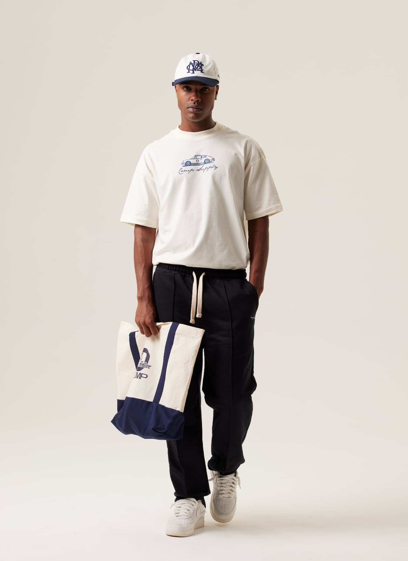 Modelo com camiseta clara, calça preta e bolsa em fundo neutro