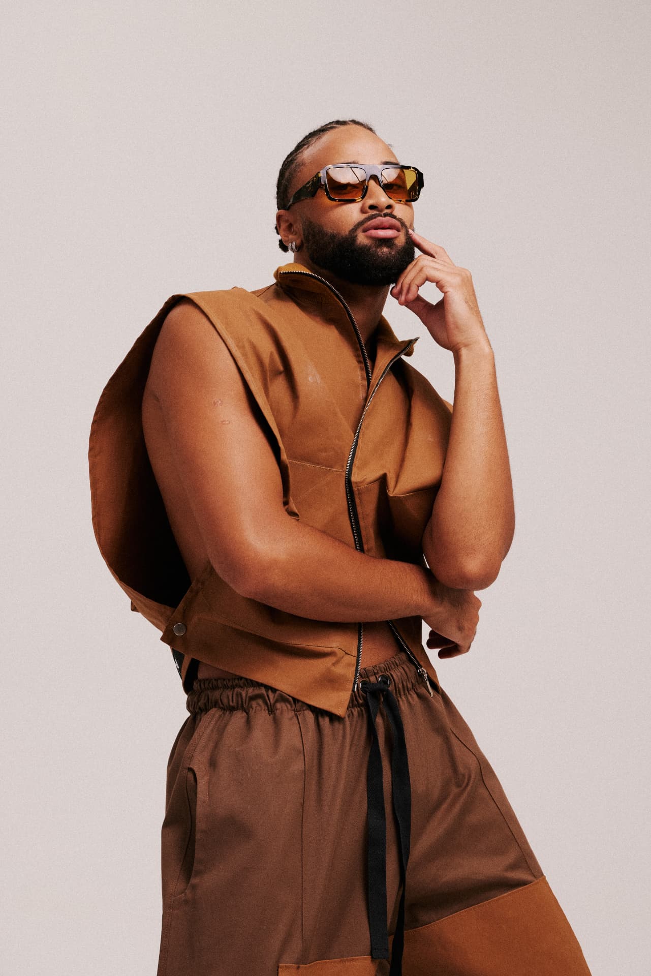 Modelo com look marrom e óculos em fundo neutro