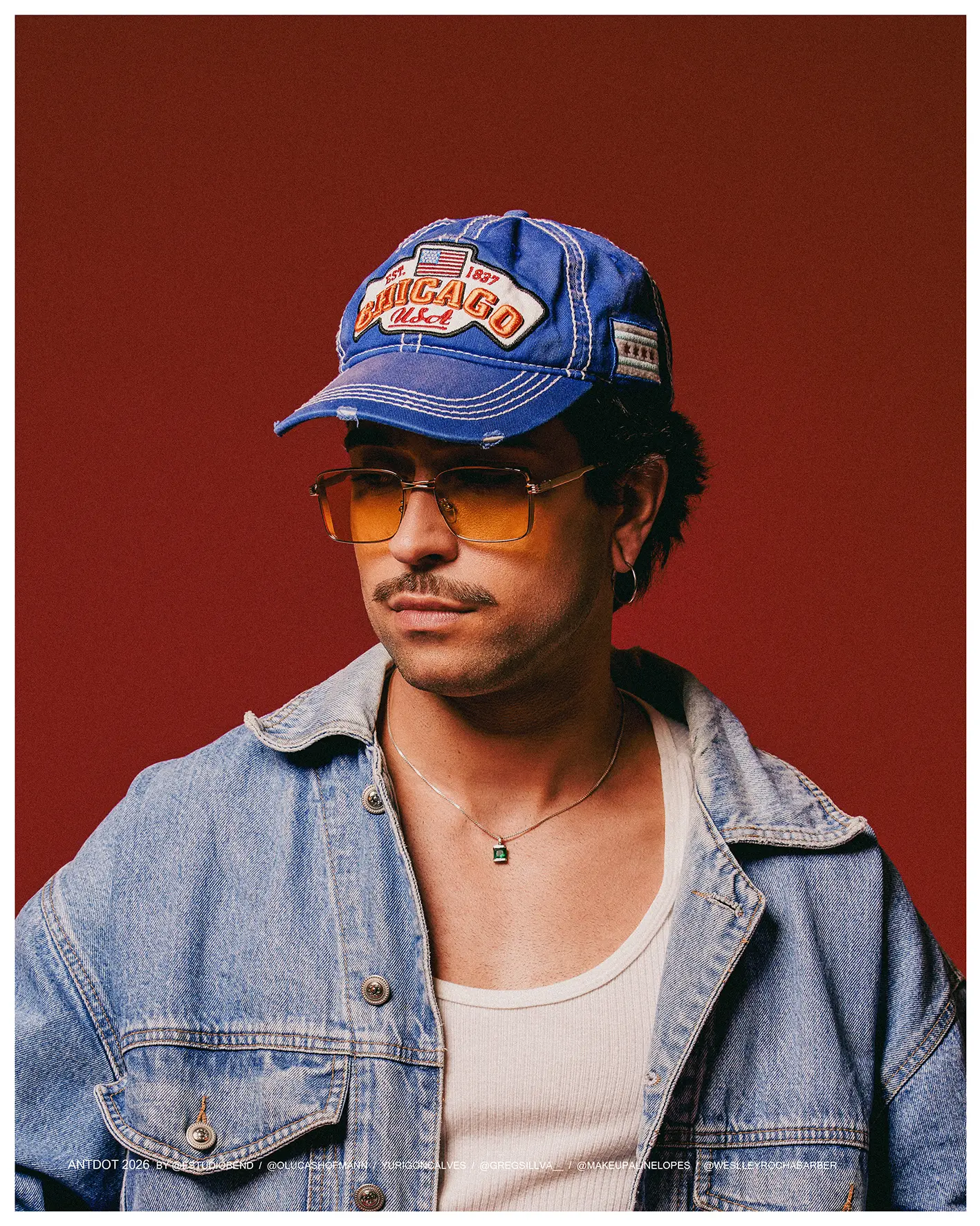 Antdot com boné Chicago, jaqueta jeans e óculos laranja em fundo vermelho
